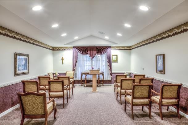 A small chapel interior with rows of chairs facing an altar, illuminated by ceiling lights.