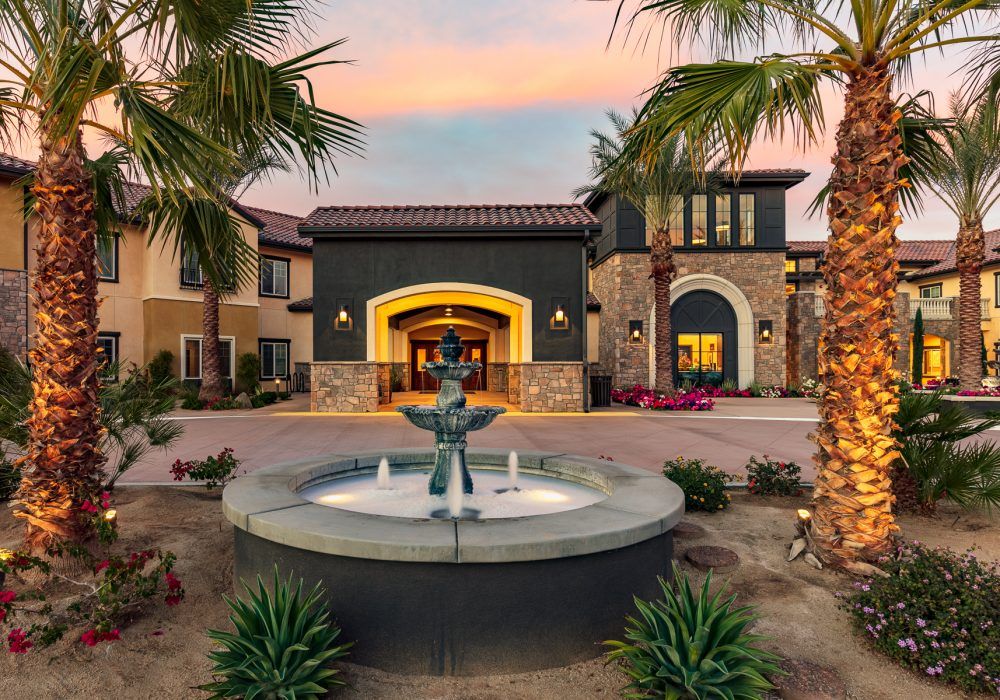 A beautiful building with a central fountain and palm trees at sunset.