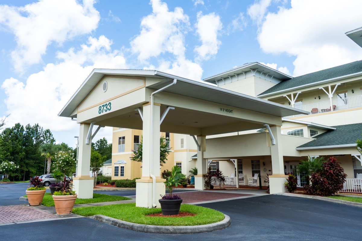 The image shows the exterior entrance of a building with a covered driveway and landscaped surroundings.