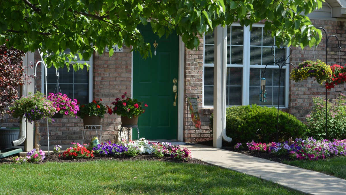 A charming brick house with a green door, surrounded by a well-maintained garden and colorful flowers.
