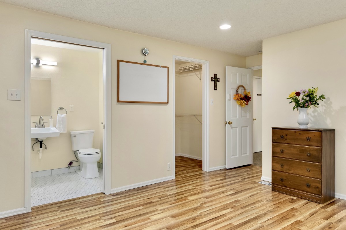 A hallway with wooden flooring featuring a bathroom, closet, and decorated door.