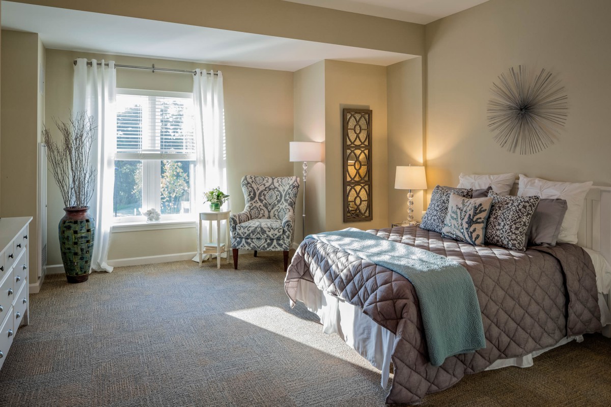 A cozy bedroom with natural light streaming through a large window, featuring elegant decor and a comfortable bed.
