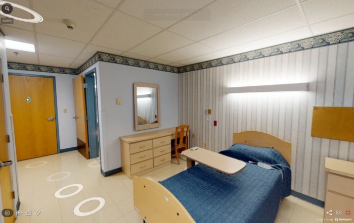 A hospital room with a bed, dresser, and mirror in a medical facility.