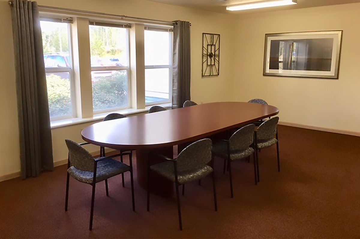 A conference room with a large oval table and several chairs around it, illuminated by natural light from the windows.
