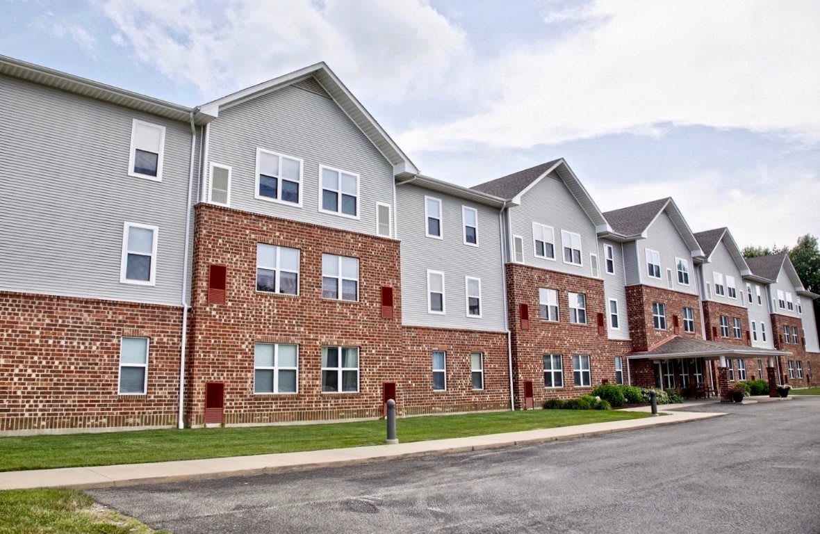 A three-story residential apartment building with a brick facade and multiple windows under a cloudy sky.