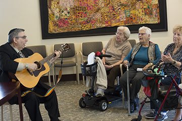 A musician plays the guitar for a group of seniors in a community setting.