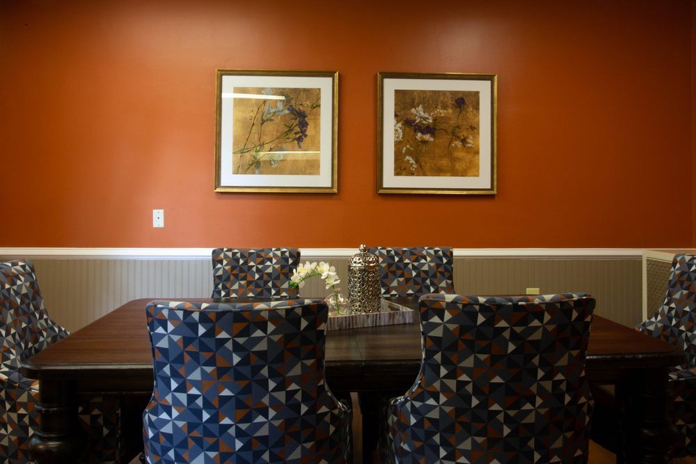A stylish dining room with patterned chairs and framed artwork on an orange accent wall.