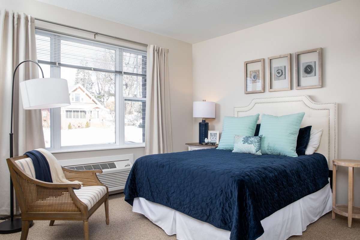 A cozy and stylish bedroom with a large window, featuring blue bedding and elegant decor.