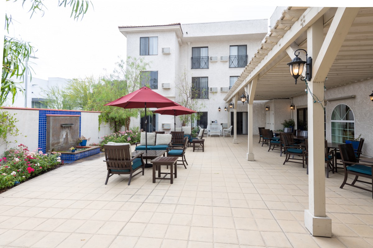 A spacious outdoor patio with tables and chairs, featuring a red umbrella and adjacent building.