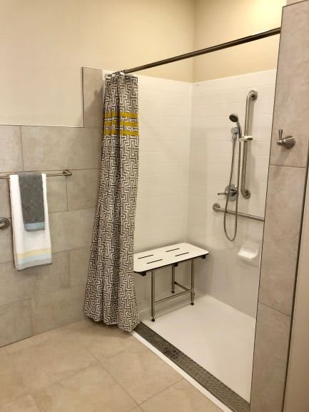 An accessible bathroom with a walk-in shower, equipped with handrails and a bench.
