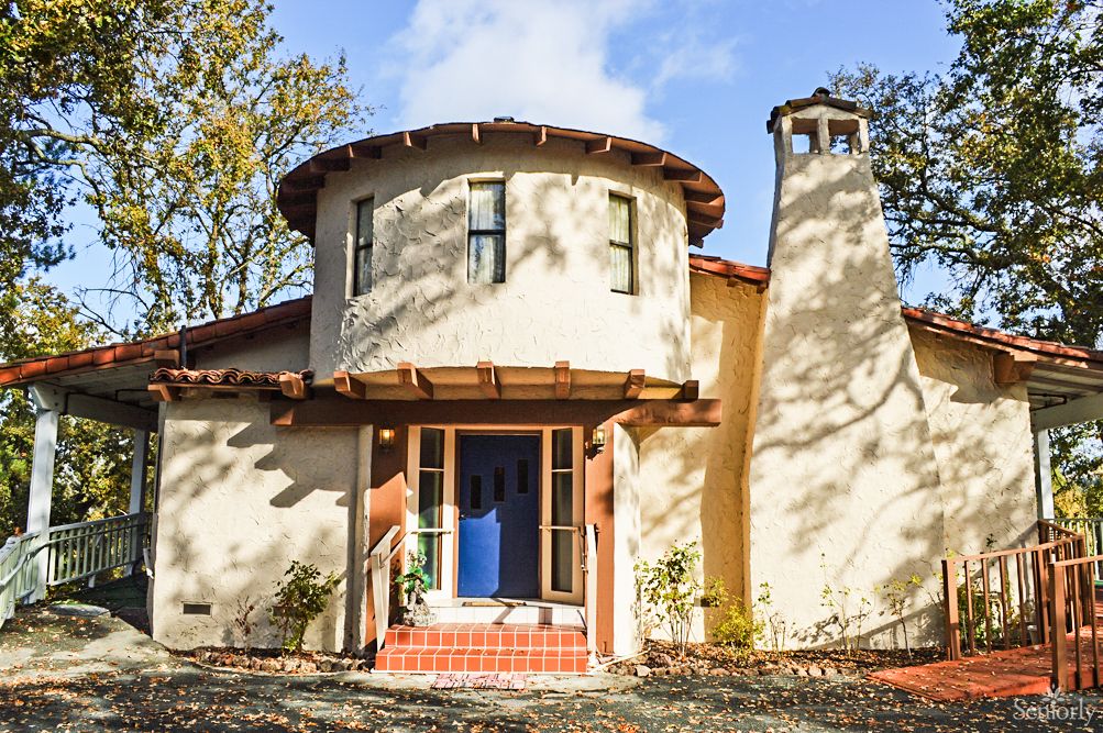 A unique house with a round tower, chimney, and blue door bathed in sunlight.