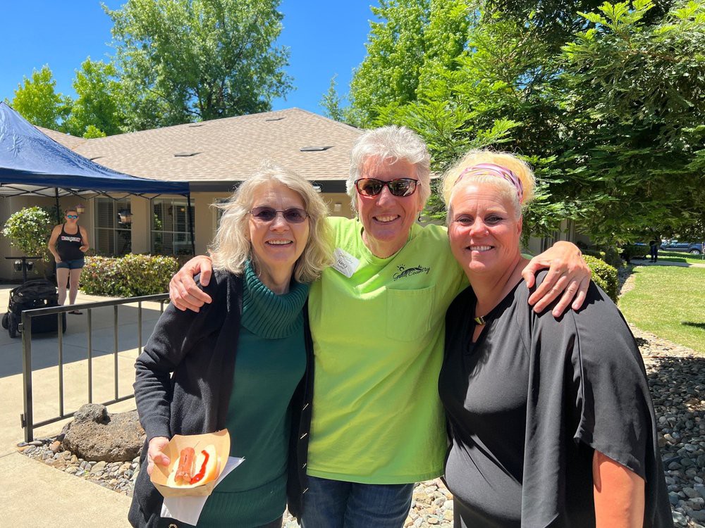 A cheerful group of three people posing together outdoors on a sunny day.