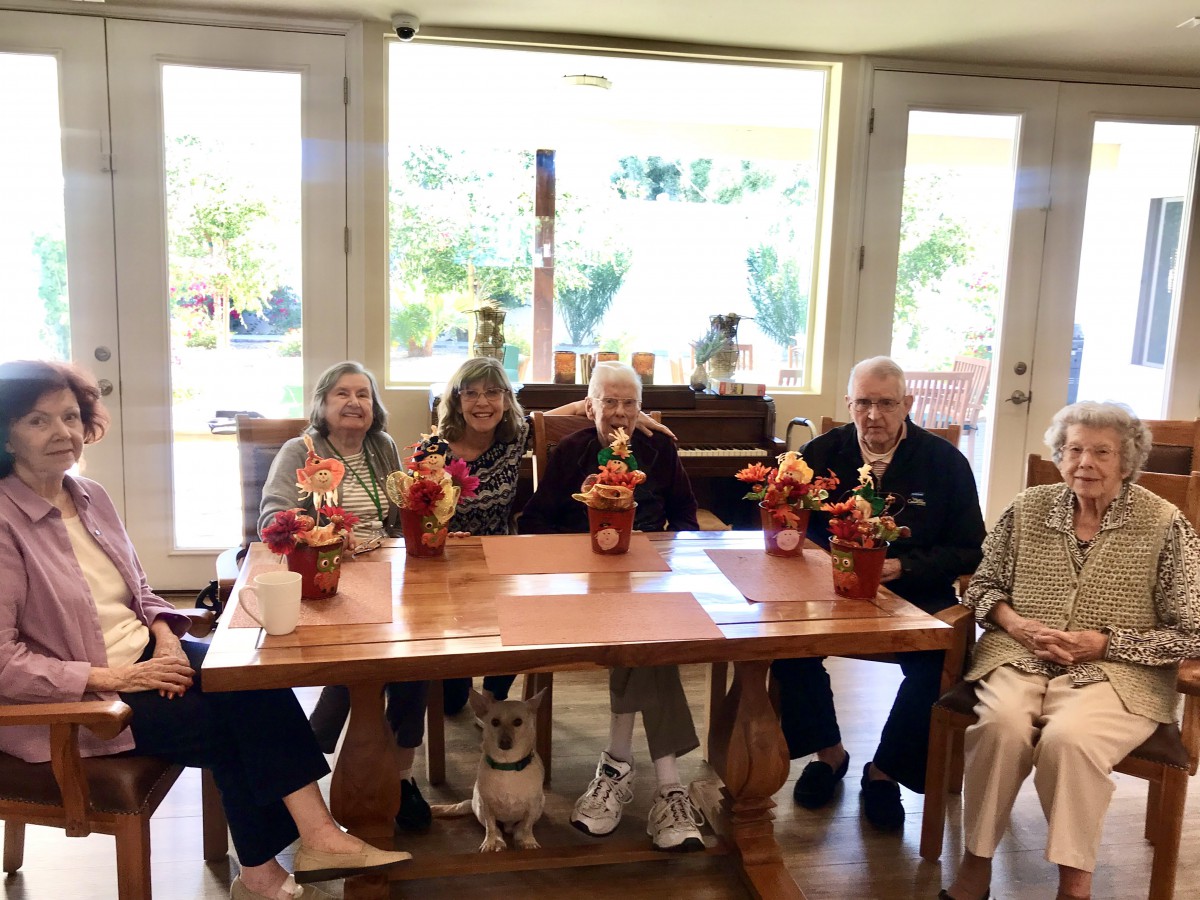 A group of adults sitting around a wooden table with flower decorations in an indoor setting.