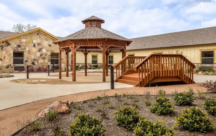 A wooden gazebo in a landscaped garden area next to a building.