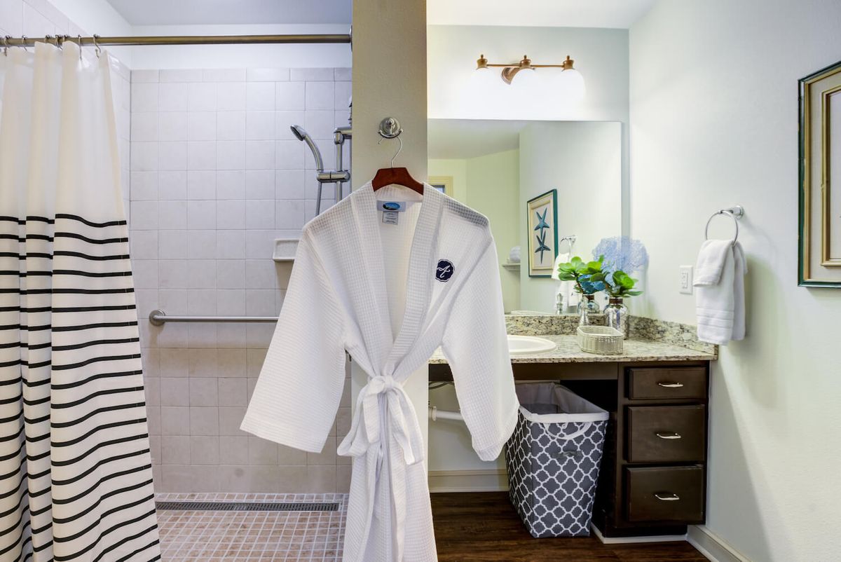 A cozy bathroom with a white robe hanging near the sink and fresh flowers on the counter.