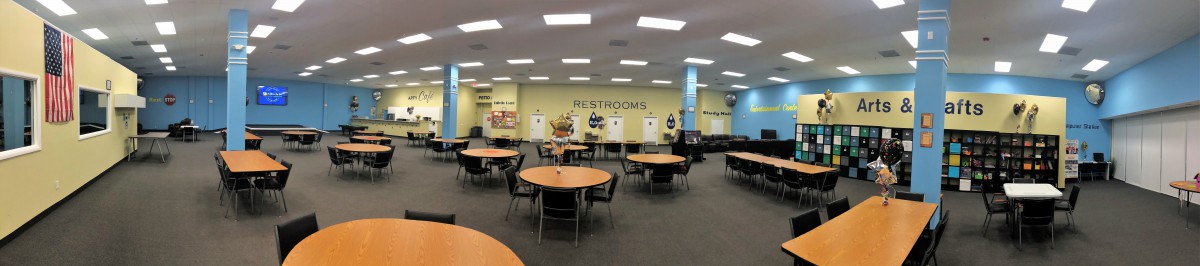 A spacious cafeteria area with round tables and restroom signs on the wall.