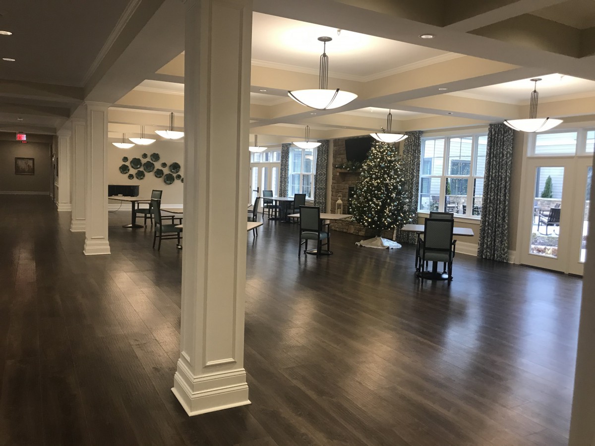 A spacious, elegantly decorated room with wooden floors, chandeliers, and arranged tables and chairs.
