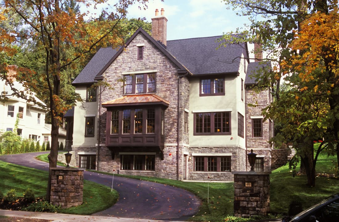 A historic stone house with a paved driveway and surrounding trees.