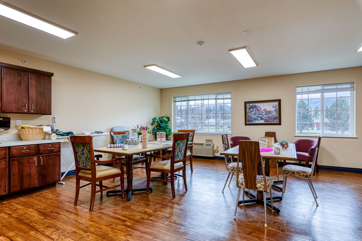 A bright dining room with several tables and chairs, featuring large windows and artwork on the walls.