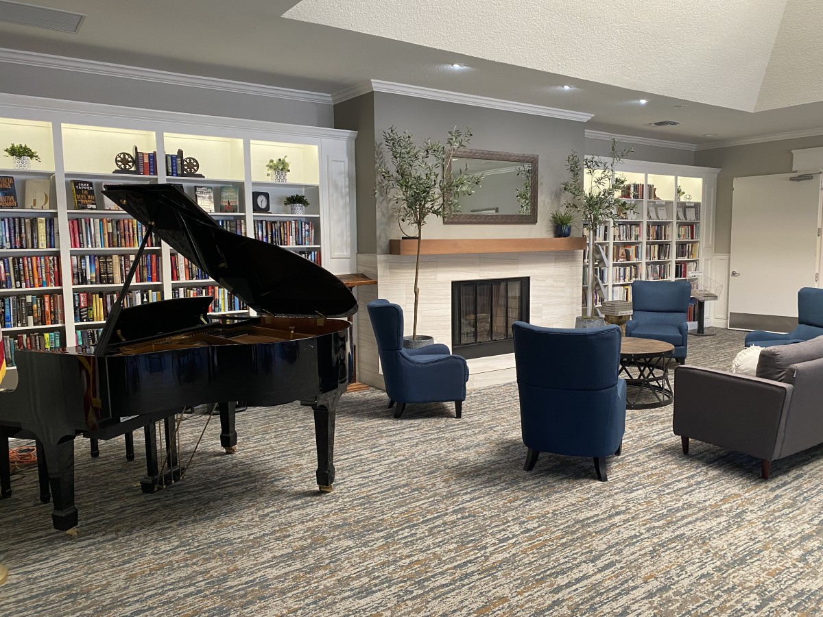 A cozy lounge area featuring a grand piano, bookshelves, and comfortable seating around a fireplace.