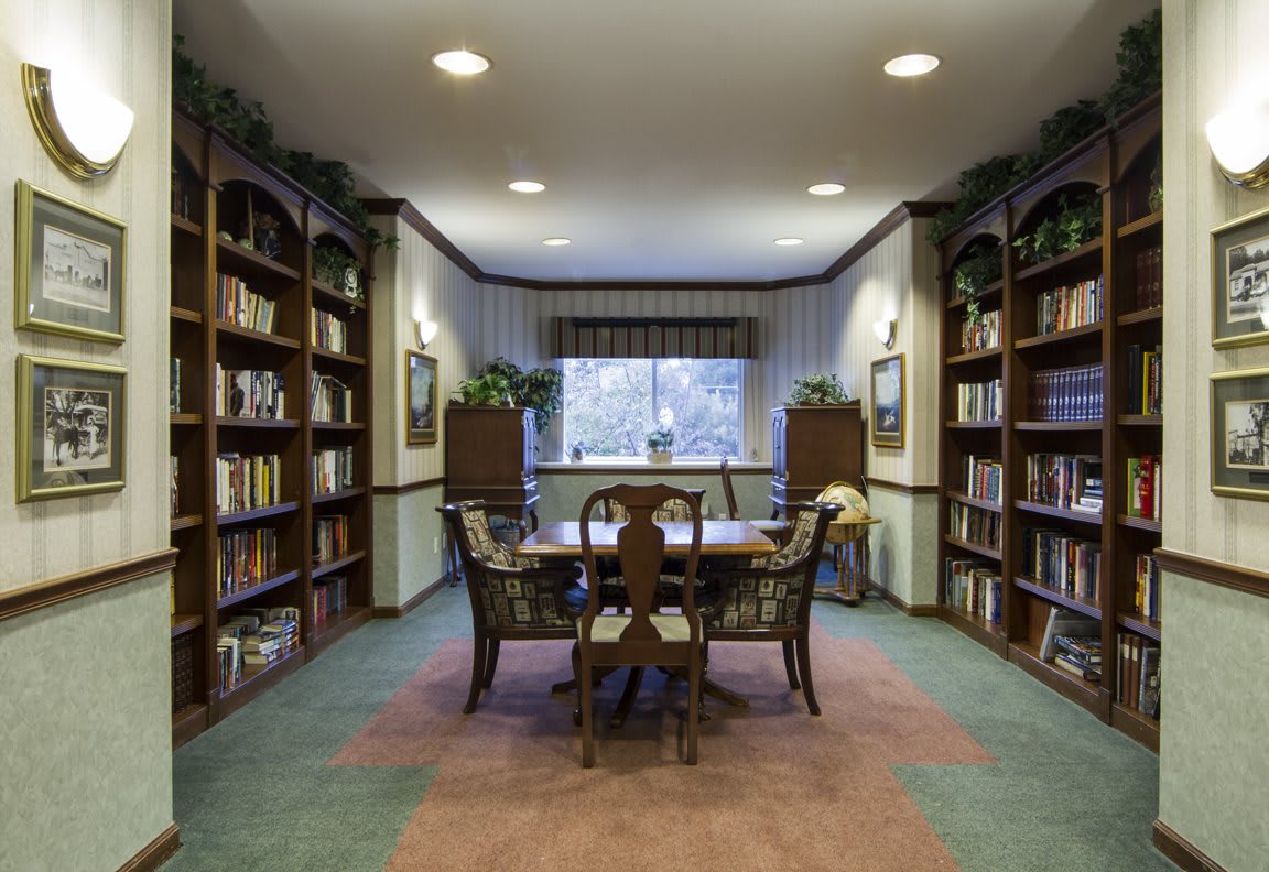 A cozy library reading room with bookshelves lining the walls and a table with chairs in the center.