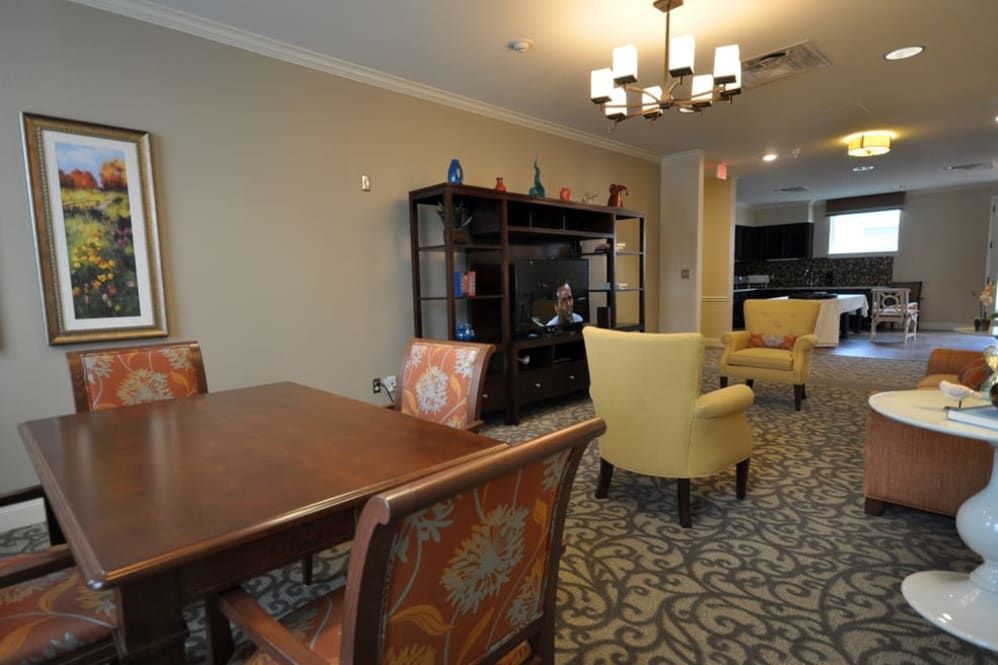 A cozy living and dining area featuring a wooden dining table, upholstered chairs, a bookshelf, and a television.