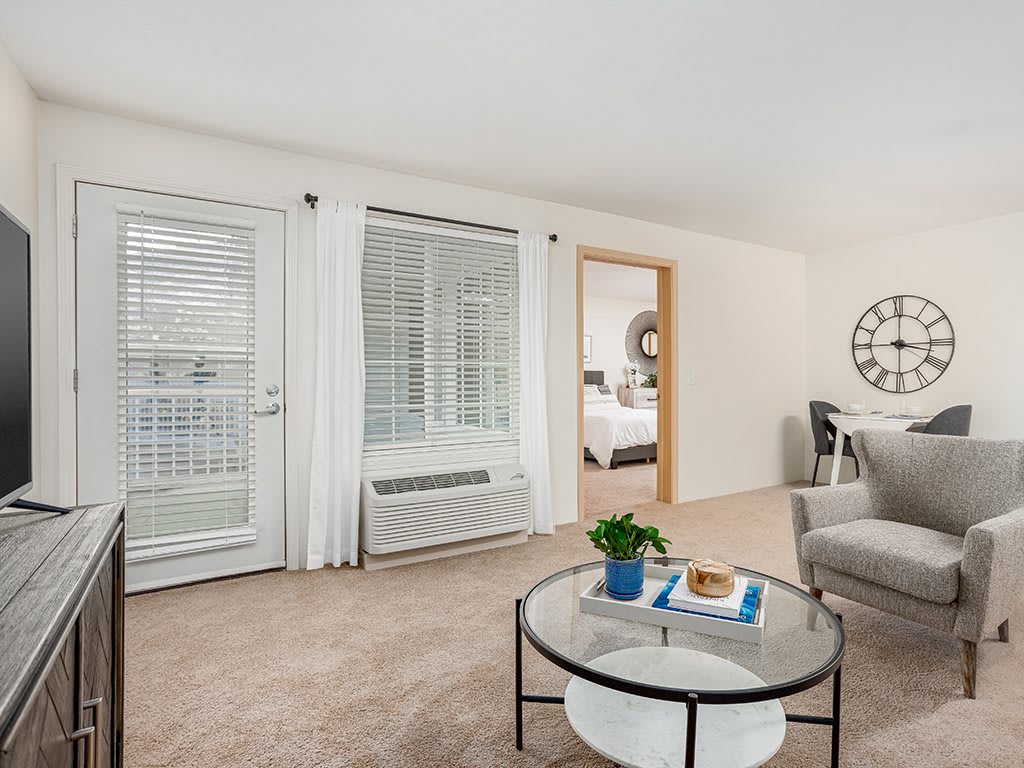 A cozy living room with neutral tones, featuring a comfortable sofa, a round glass coffee table, and elegant curtains.
