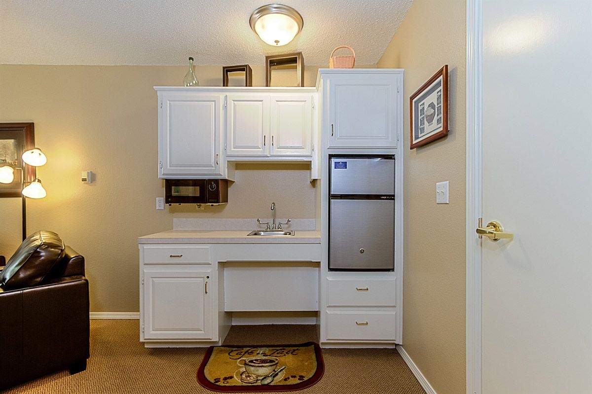 A small kitchenette with white cabinets and a compact fridge, set against beige walls.
