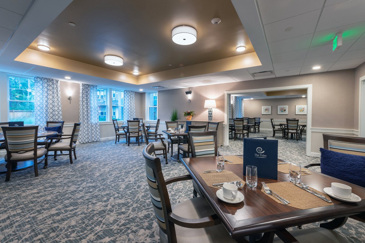 A cozy dining room with neatly arranged tables and chairs, featuring elegant lighting and decor.