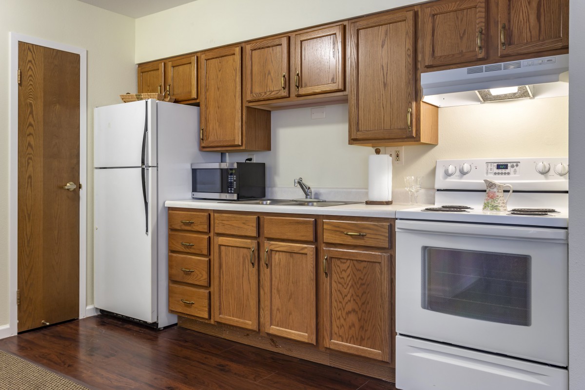 A modern kitchen with wooden cabinets, a refrigerator, stove, and microwave.