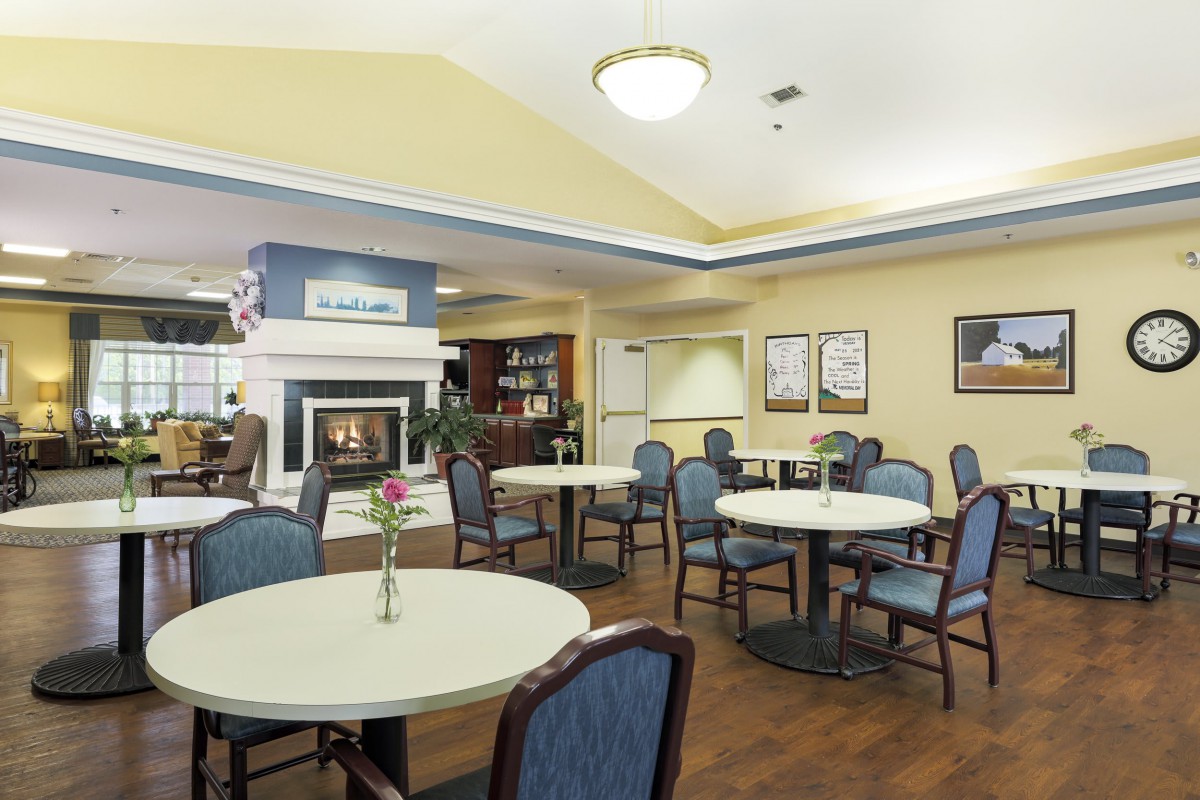 A cozy dining area with tables and chairs, featuring a fireplace and warm lighting.