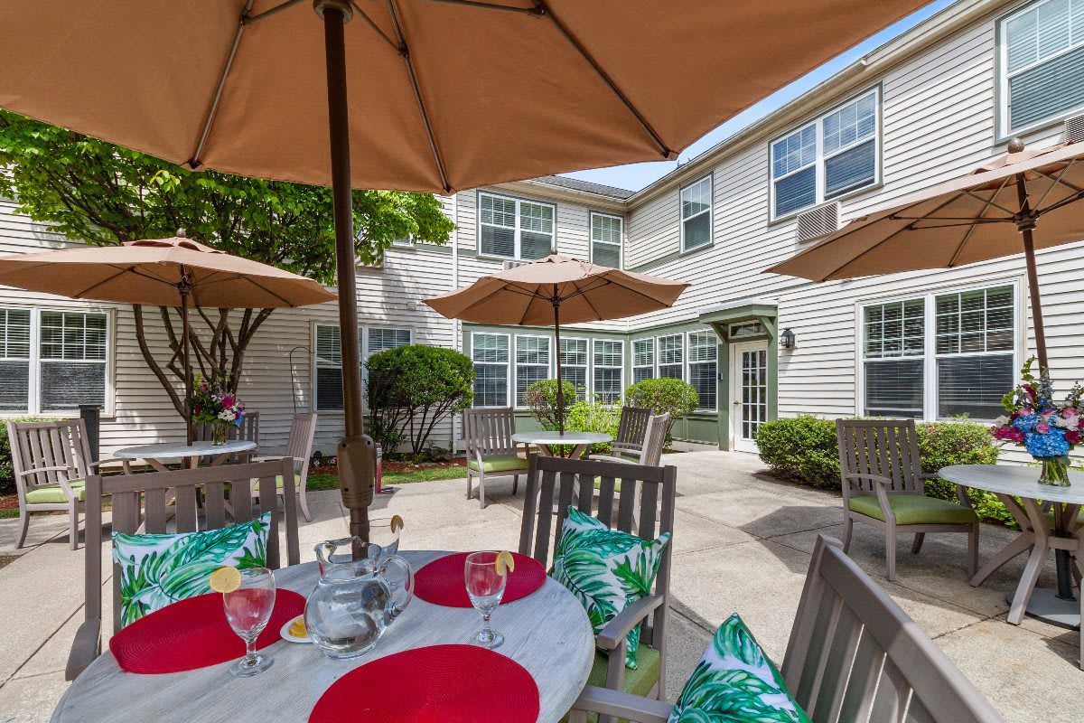 A cozy outdoor patio with tables, chairs, and umbrellas in a garden setting.