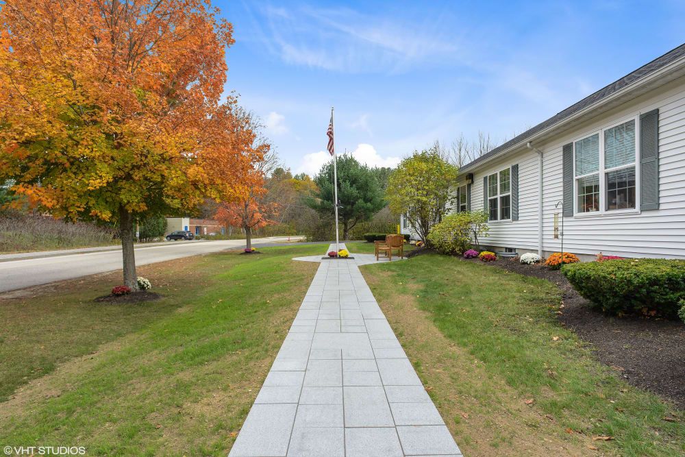 A paved walkway leading to a house with trees showing autumn colors.