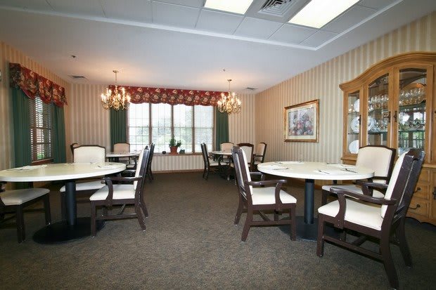 A spacious and elegantly decorated dining room with multiple tables and chairs, featuring chandeliers and a large window.