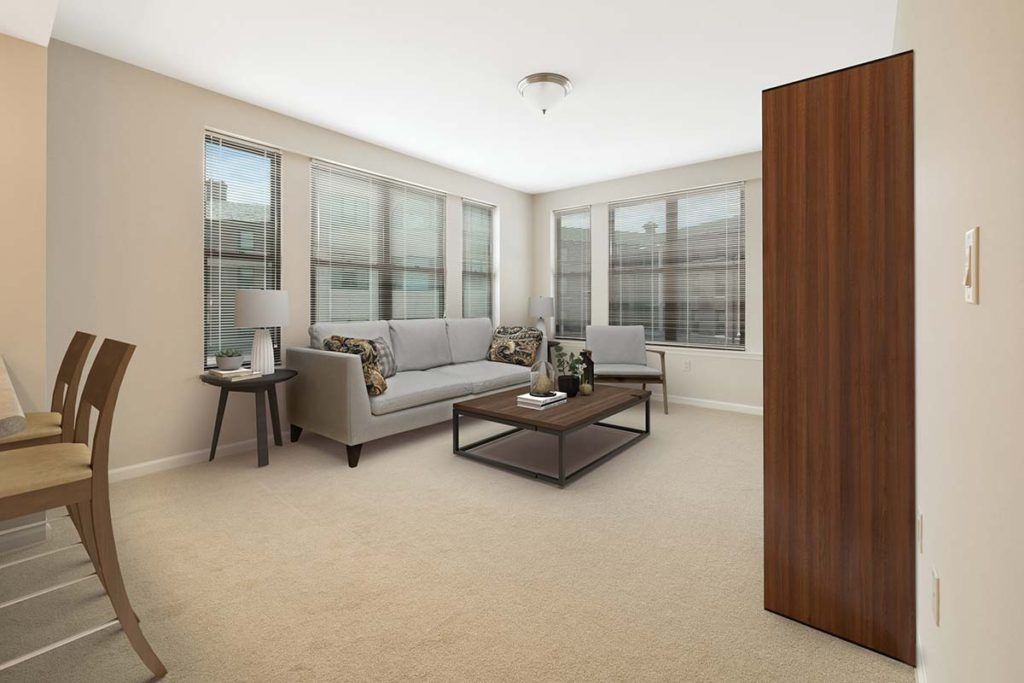 A modern living room with a gray sofa, coffee table, armchair, and large windows letting in natural light.