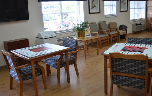 A cozy waiting area featuring wooden tables and chairs, illuminated by natural light from a nearby window.