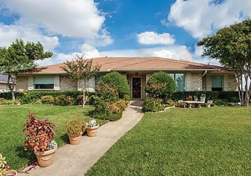 A suburban house with a well-maintained lawn and garden under a bright blue sky.