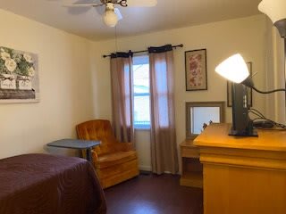 A cozy bedroom with a desk, chair, and window with curtains.