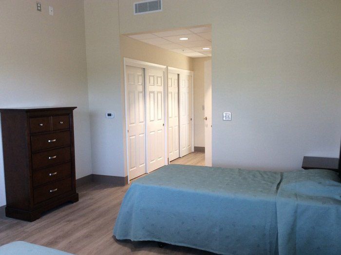 A bedroom featuring a bed with a blue bedspread, a wooden dresser, and a view of the hallway leading to closets.