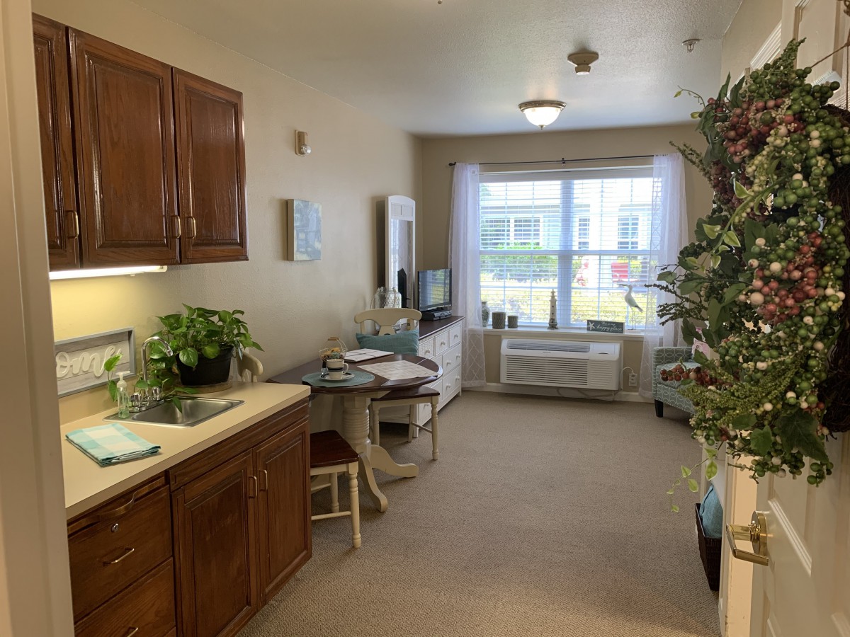 A cozy apartment kitchen area with wooden cabinets, a small table, and a window letting in natural light.