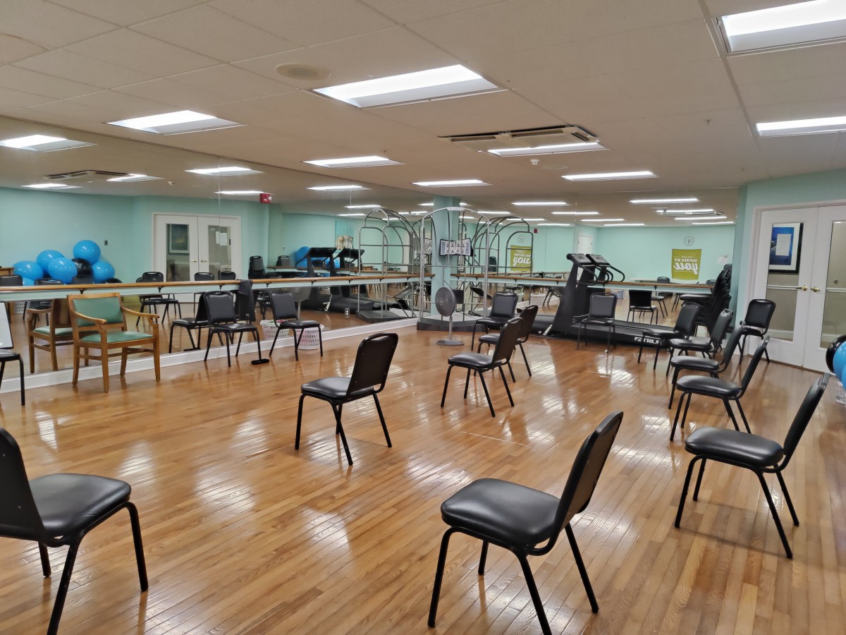 A spacious gym with chairs arranged and various exercise equipment in the background.