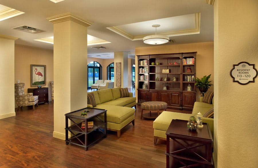 A modern living room with plush green sofas, a wooden bookshelf, and warm lighting.