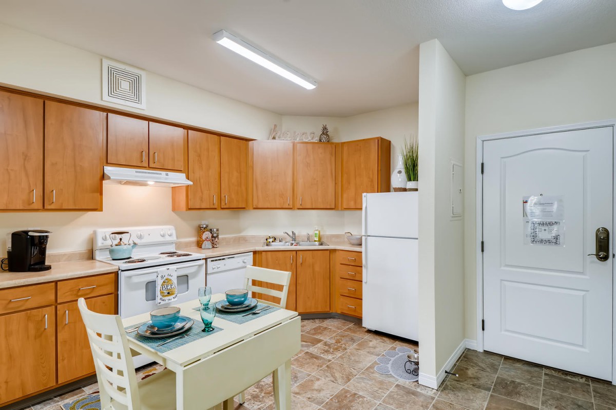A compact kitchen with wooden cabinets, a small dining table set, and standard appliances including a refrigerator and stove.
