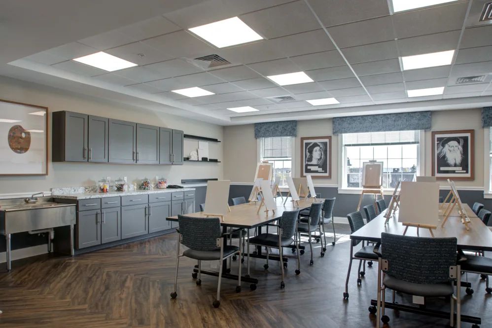 A spacious art classroom with desks and easels, well-lit by large windows.