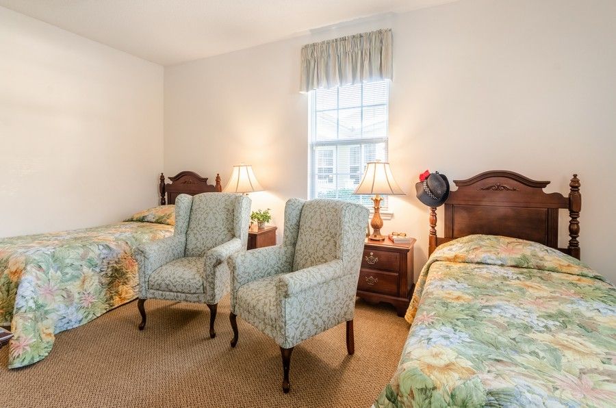 A cozy bedroom with two beds, armchairs, and warm lighting.