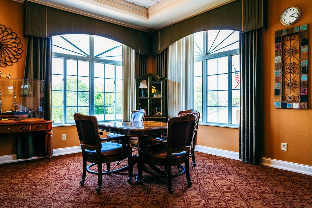 A cozy dining room with a round table, chairs, large windows, and elegant curtains.