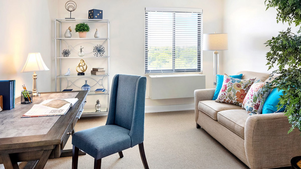 A bright and modern office space with a blue chair, beige sofa, decorative shelves, and a large window.