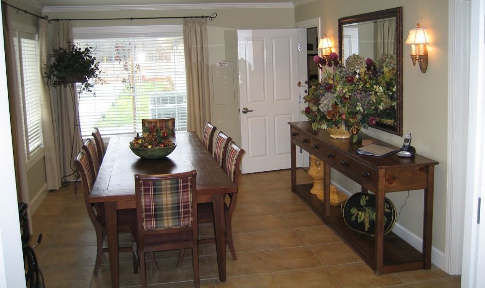 A cozy dining room with a wooden table and chairs, decorated with plants and a large mirror.