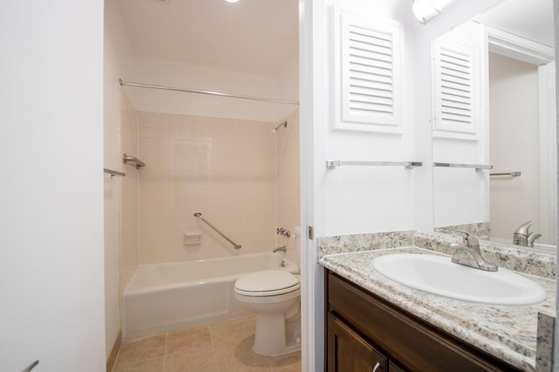 A well-lit bathroom featuring a bathtub, toilet, and a sink with a granite countertop.