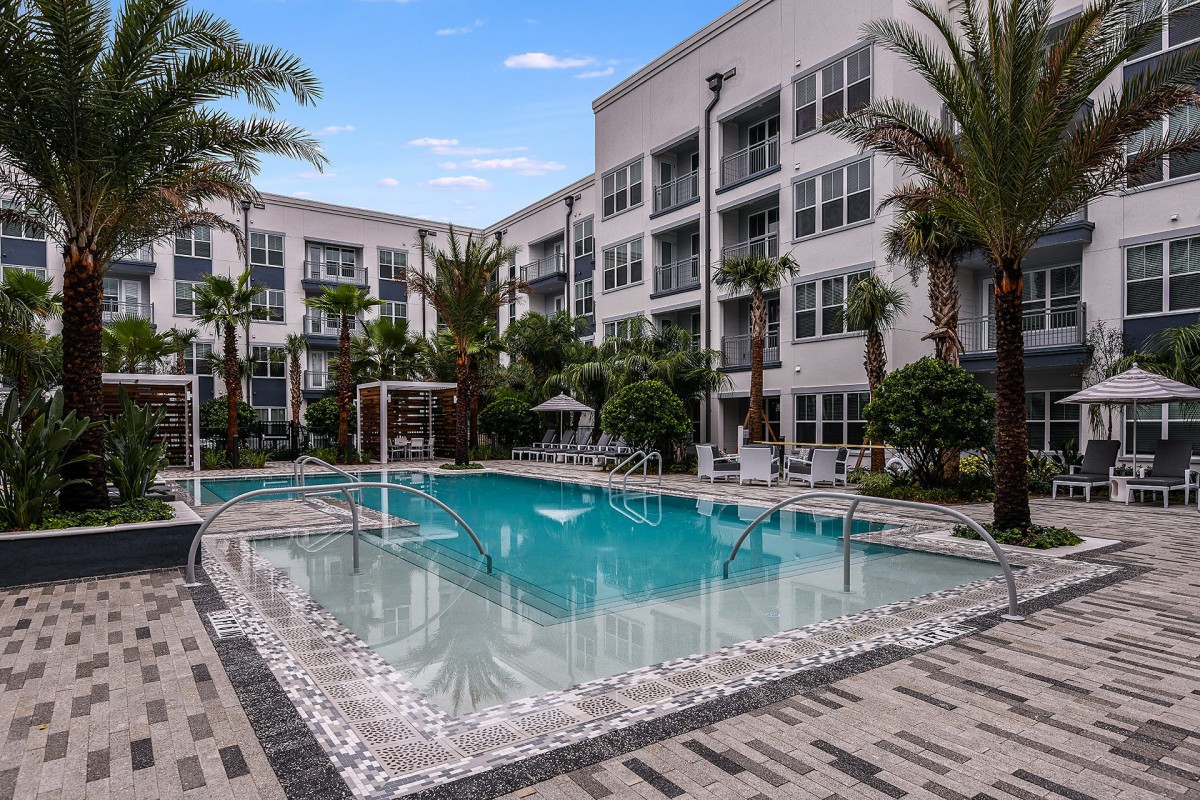 A luxurious apartment complex with a refreshing outdoor swimming pool surrounded by palm trees.